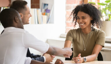 A young person shaking hand with a person on the opposite side of the table in an office setting.