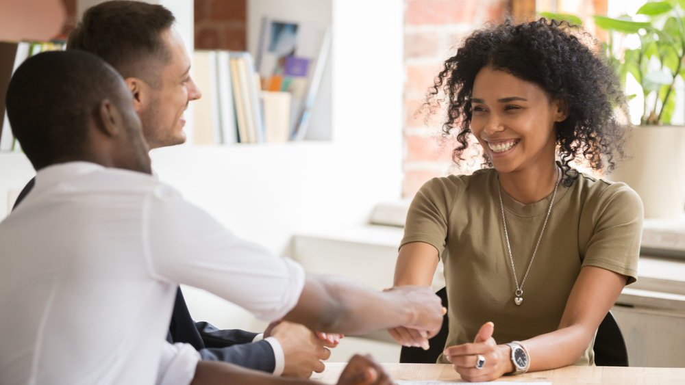 A young person shaking hand with a person on the opposite side of the table in an office setting.