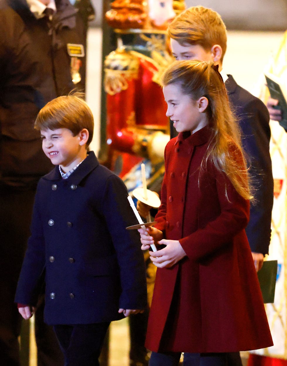 children in formal attire holding a small object walking in an indoor setting with decorative elements in the background