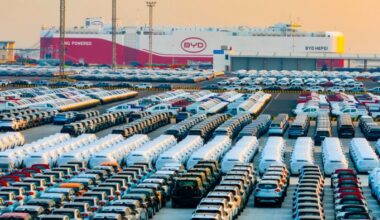Rows of new energy vehicles are parked at a port terminal, with the BYD Hefei ro-ro ship in the background preparing for export.