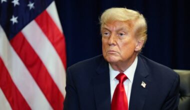 Donald Trump sits in front of an American flag, wearing a dark suit and red tie, during a meeting at the United Nations General Assembly.