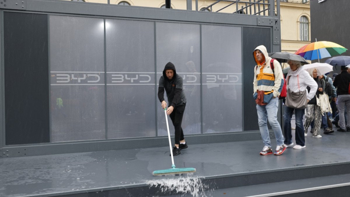 A staff member sweeps water off the pavement outside the booth of Chinese car manufacturer BYD, in central Munich during the IAA Mobility International Motor Show on September 10, 2025.