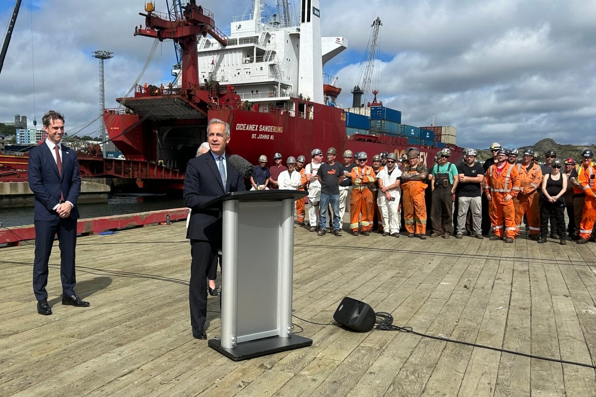 A man at a podium in front of a ship.