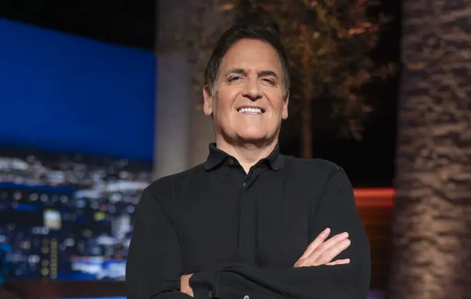 Mark Cuban in a black shirt on set smiling with his arms crossed