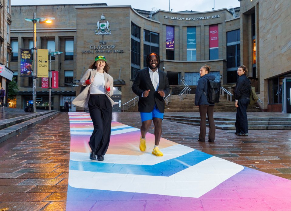 People in protective gear speed walking on a colorful Sky Fast Lane next to Glasgow's Buchanan Galleries to highlight Sky Broadband's fast internet speeds.