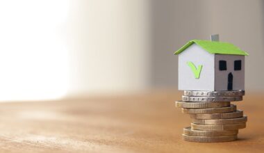 A small toy house with a green tick on the side on top of a pile of coins