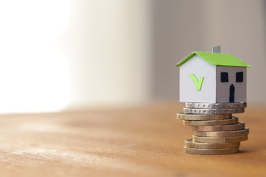 A small toy house with a green tick on the side on top of a pile of coins
