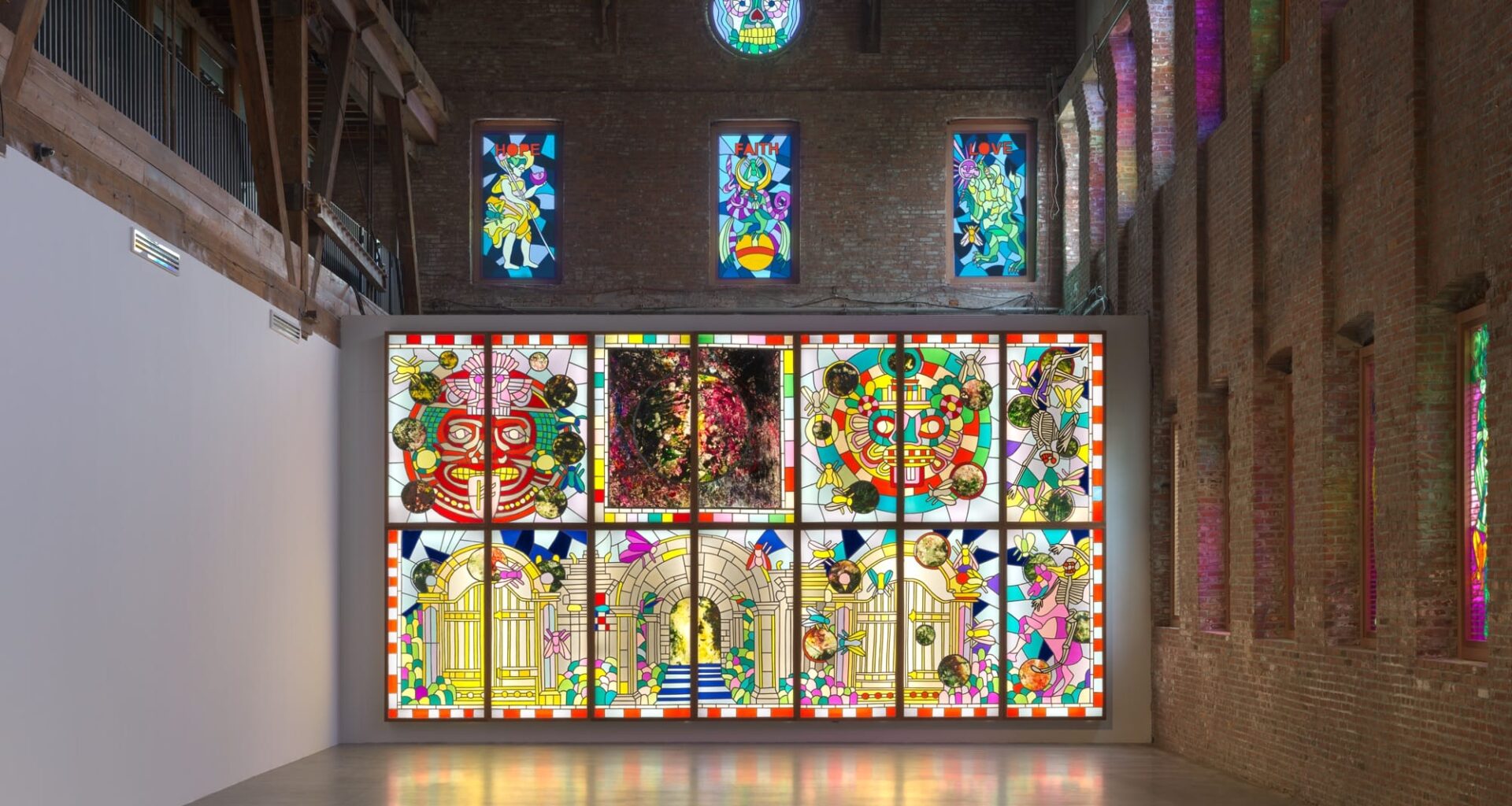 an installation by Raul de Nieves of a colorful lightbox mural with deities and skeletons along with smaller window fitted pieces