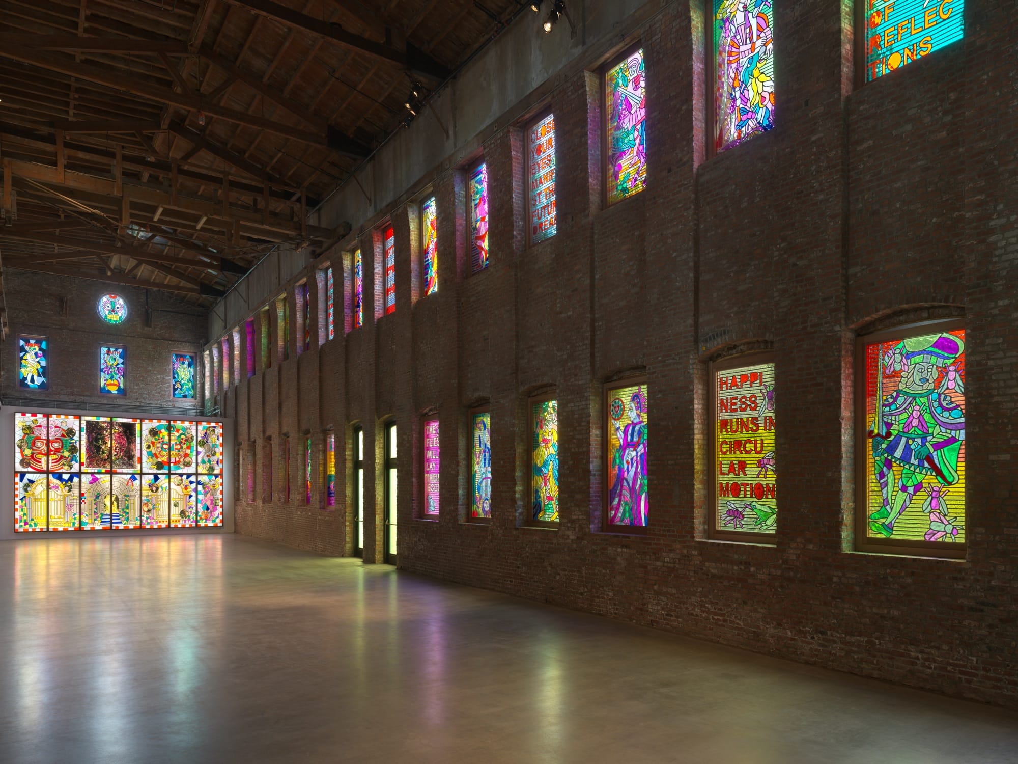 an installation by Raul de Nieves of a colorful lightbox mural with deities and skeletons along with smaller window fitted pieces