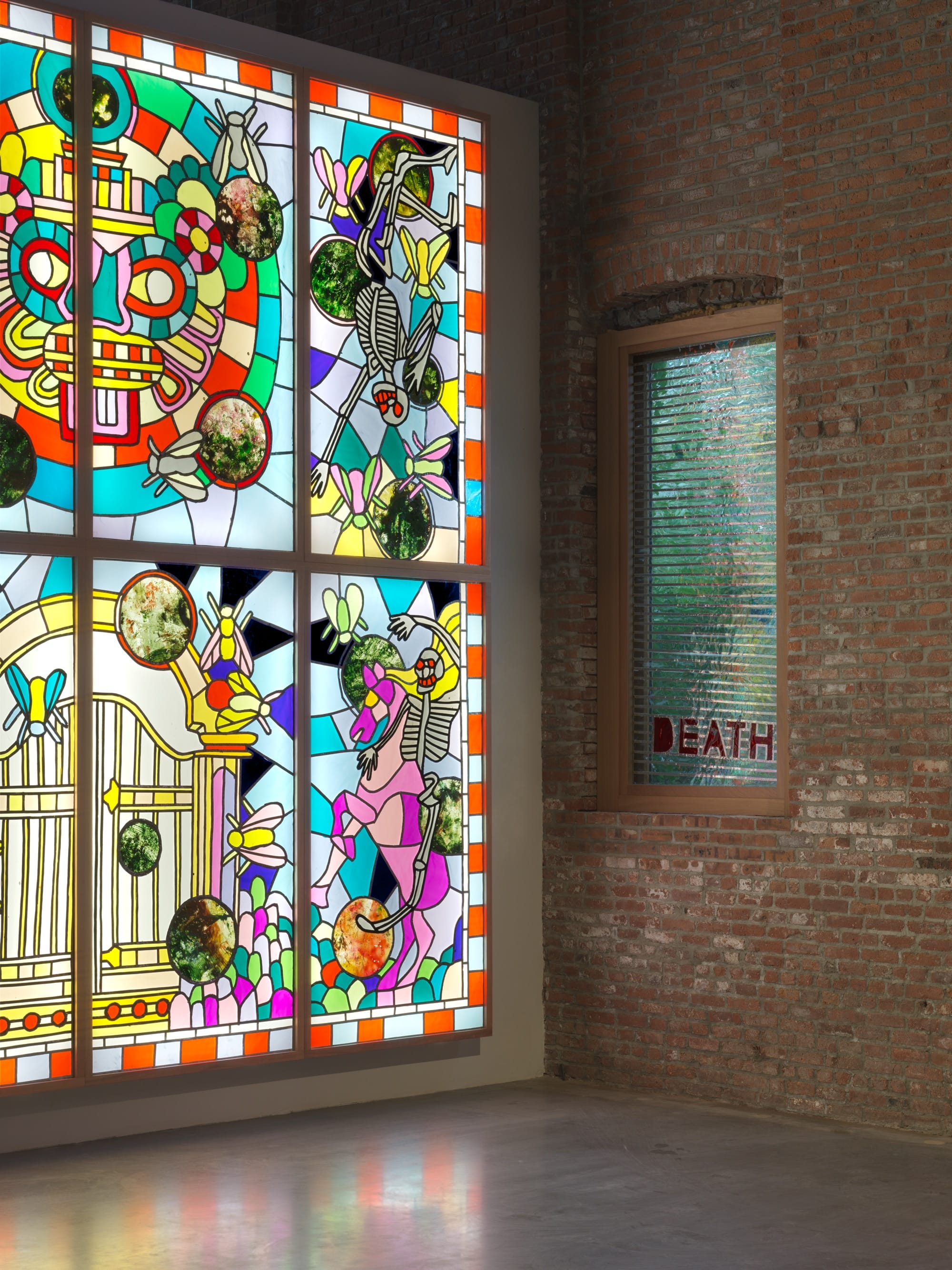 detail of an installation by Raul de Nieves of a colorful lightbox mural with deities and skeletons along with smaller window fitted pieces