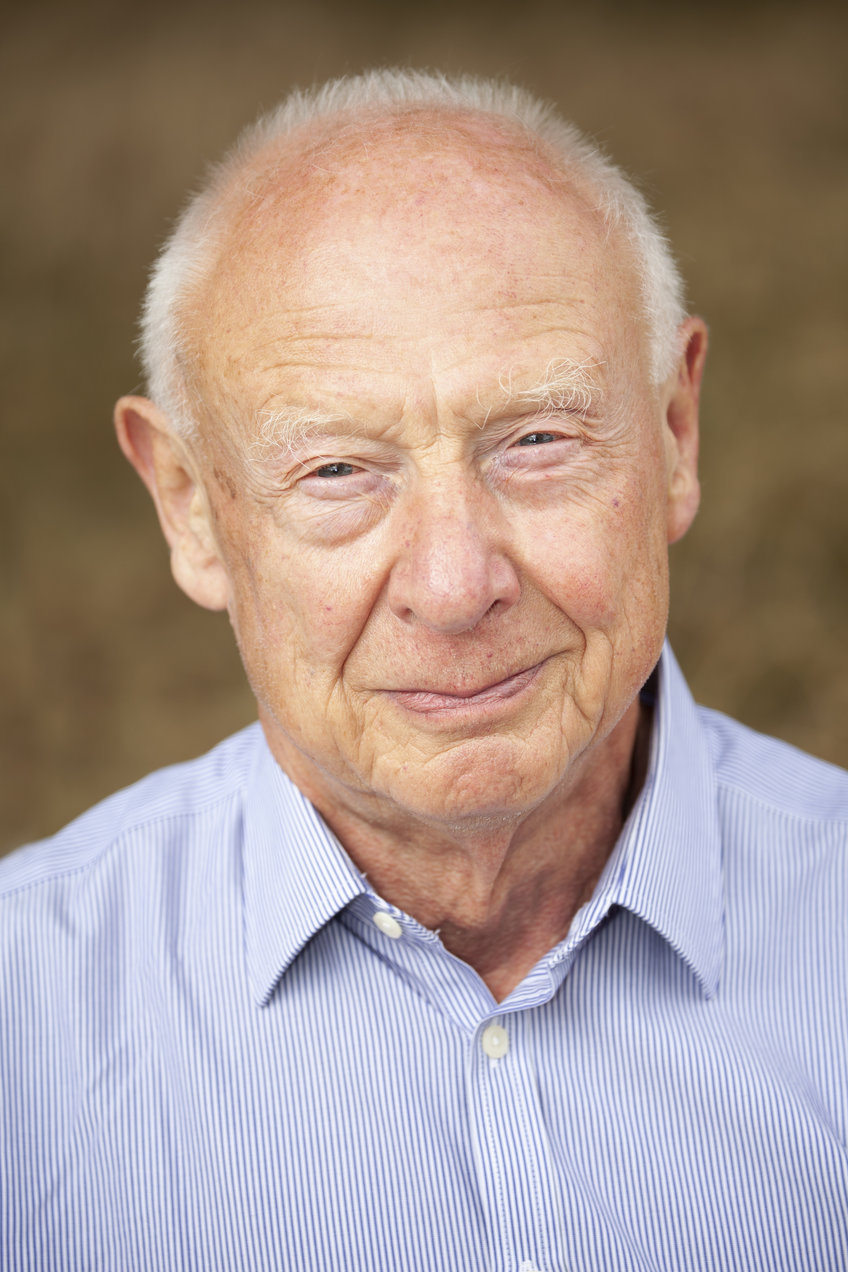 Davor Solter. An older gentleman with white hair is seen wearing a blue and white striped button-up shirt, set against a blurred neutral brown backdrop.