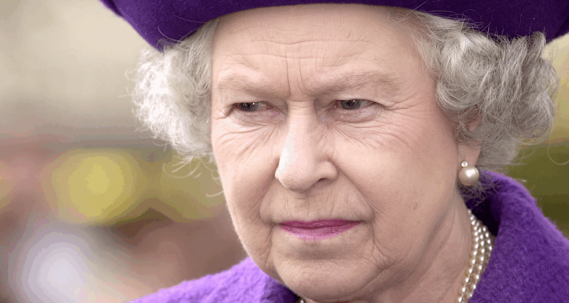 Queen Elizabeth wearing a purple hat and coat scowling