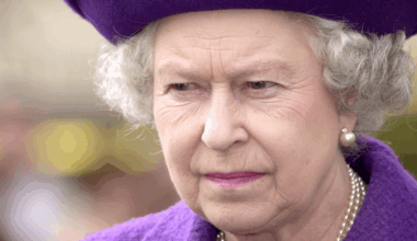 Queen Elizabeth wearing a purple hat and coat scowling