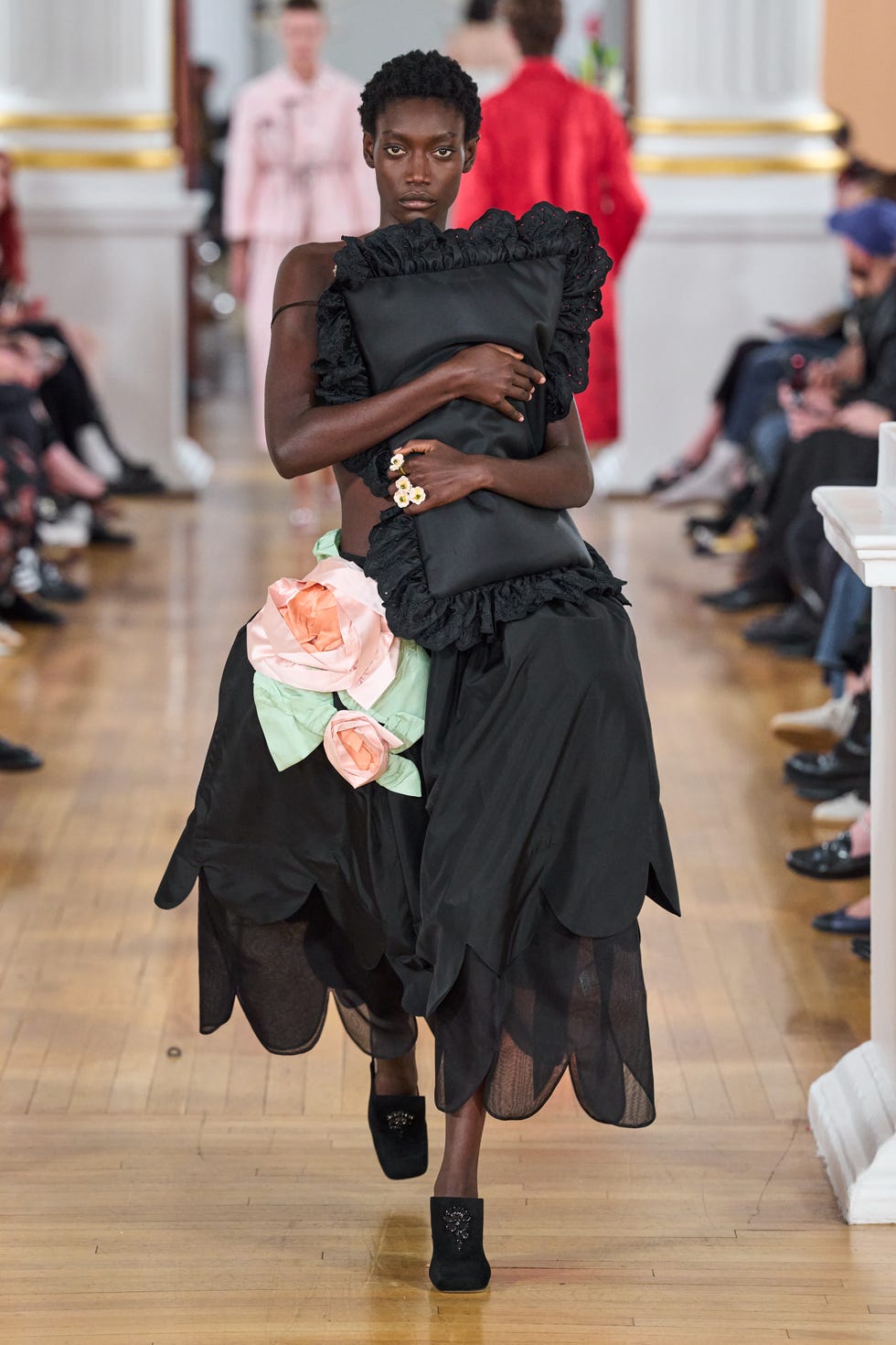 model walking down a runway wearing a unique black dress with floral accents