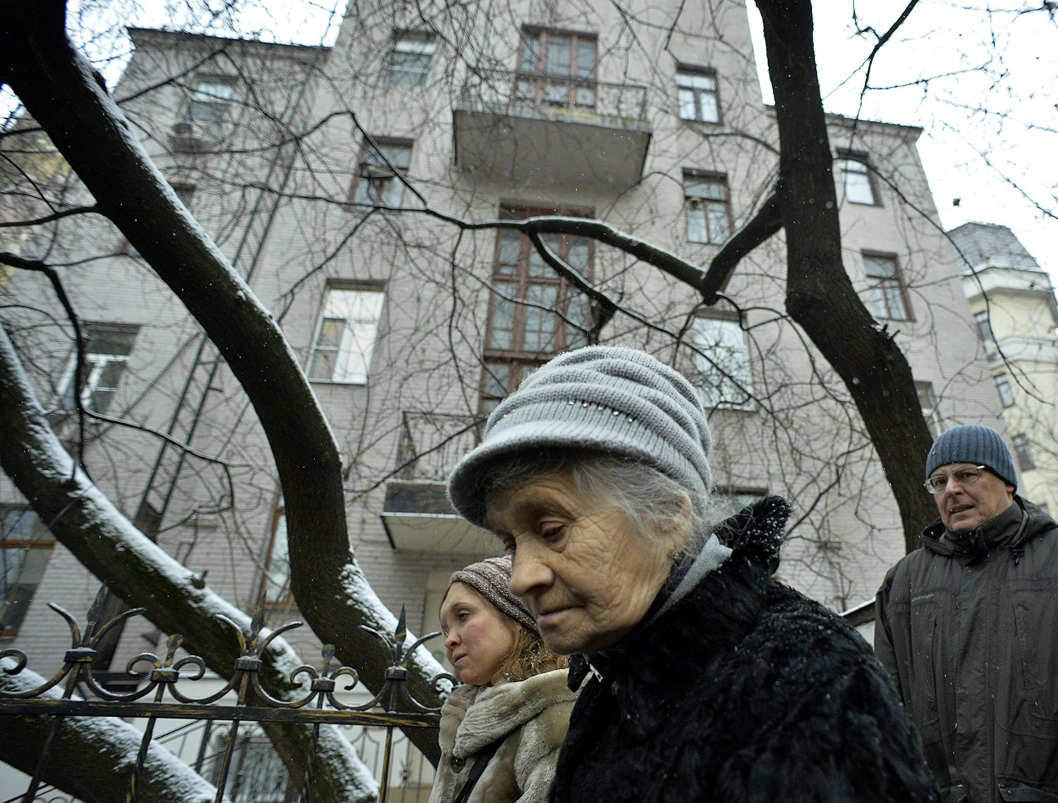 People with bowed heads wearing winter clothes pass by the bare and snowy branches of a tree in front of an apartment building in Moscow as they attend the ceremony for the installation of commemorative plaques to the victims of Soviet repression on the wall of their former house.