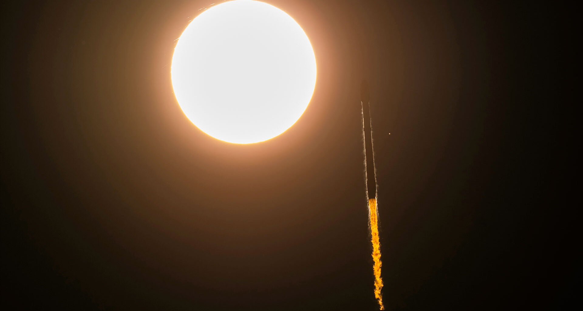 a rocket is seen in slihouette launching to space as it appears to pass by the sun