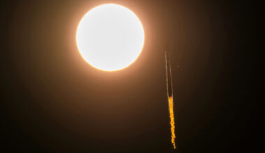 a rocket is seen in slihouette launching to space as it appears to pass by the sun
