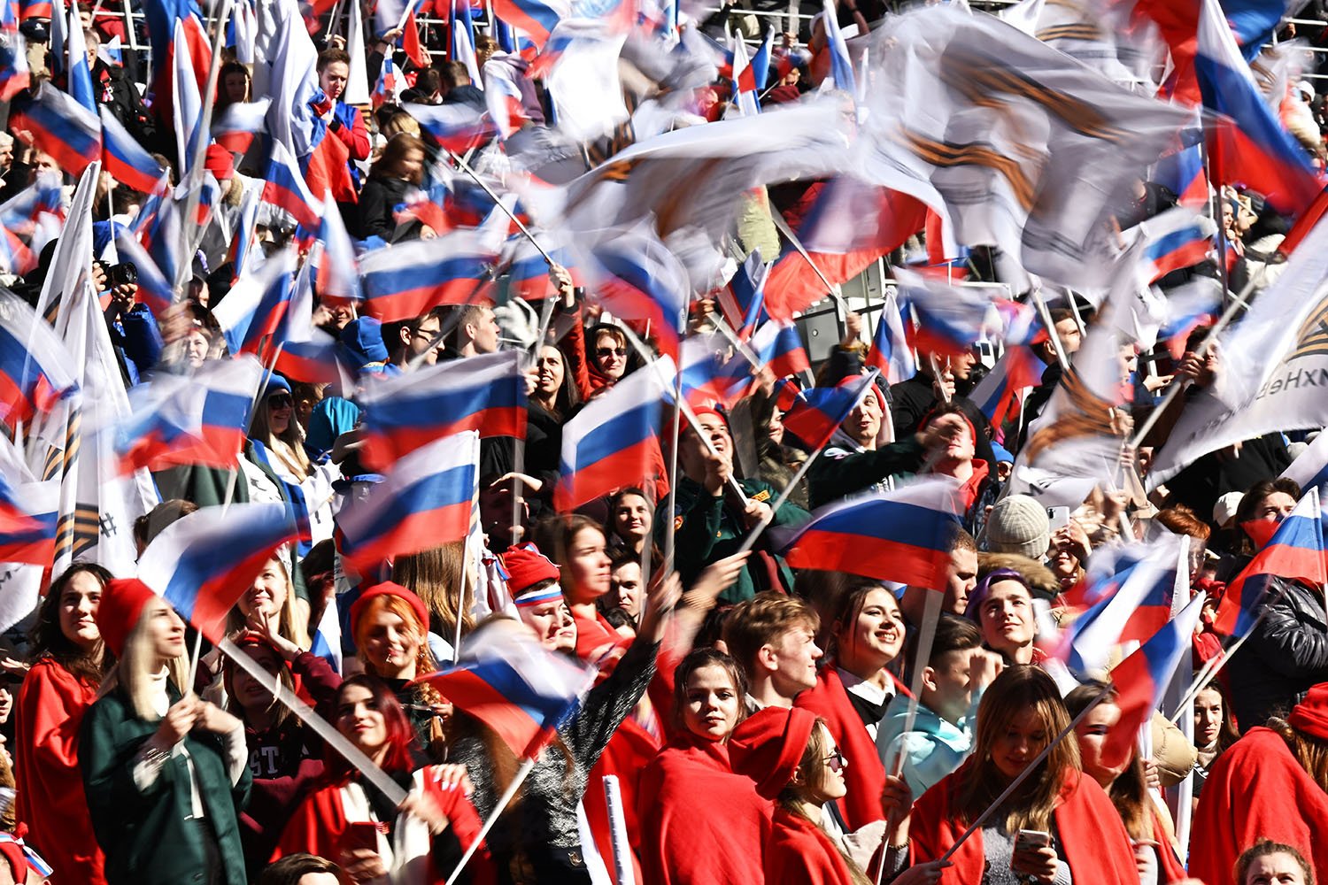 A stadium full of people, most wearing red, wave Russian flags.