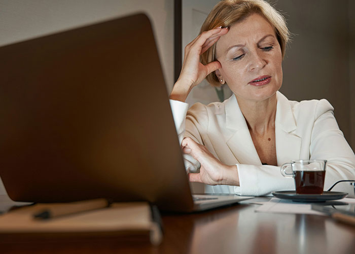 Woman in a white blazer working on a laptop, appearing thoughtful while uncovering unexpected industry secrets at night.
