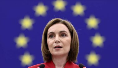 A woman speaks at a press conference with a European Union flag in the background