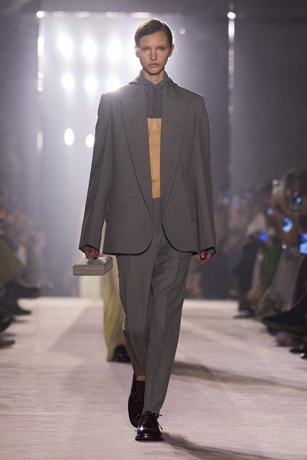 a male model walks the runway in a gray suit with a unique layered top