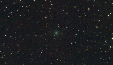 A bright green light faintly glows in the center of a dark starry night sky