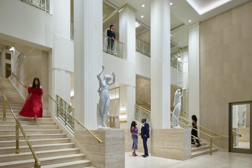 Double-height hotel foyer with travertine staircases and white figurative sculptures