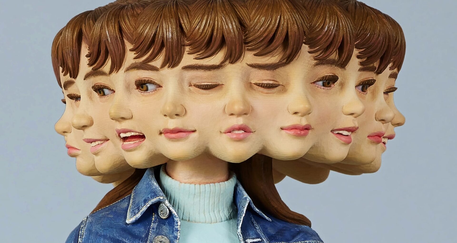a detail of a wooden sculpture by Yoshitoshi Kanemaki of a female figure with a bright pink skirt and a denim jacket, with multiple faces and expressions