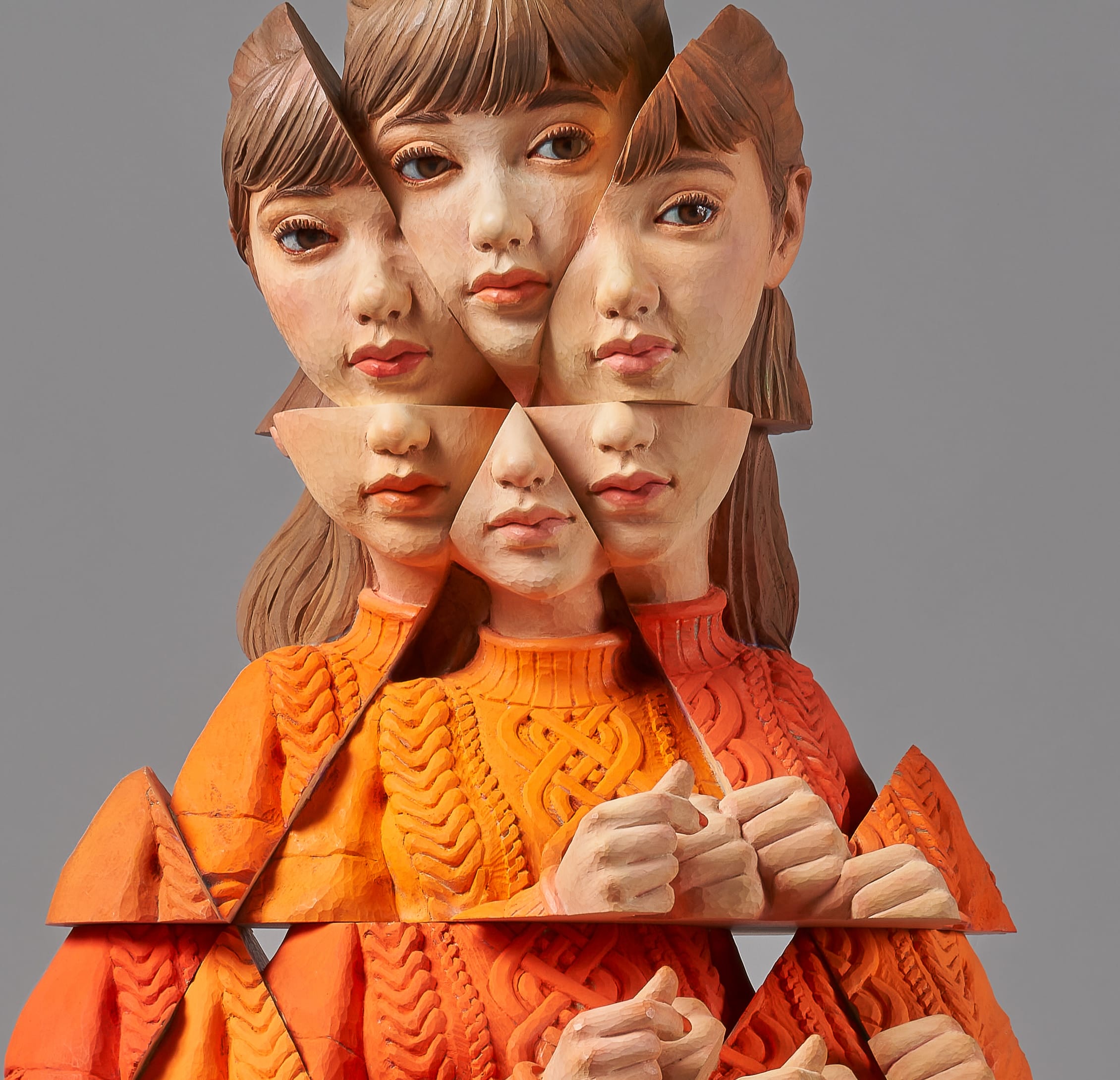 a detail of a wooden sculpture by Yoshitoshi Kanemaki of a female figure wearing an orange sweater and skirt, with prismatic or fragmented features