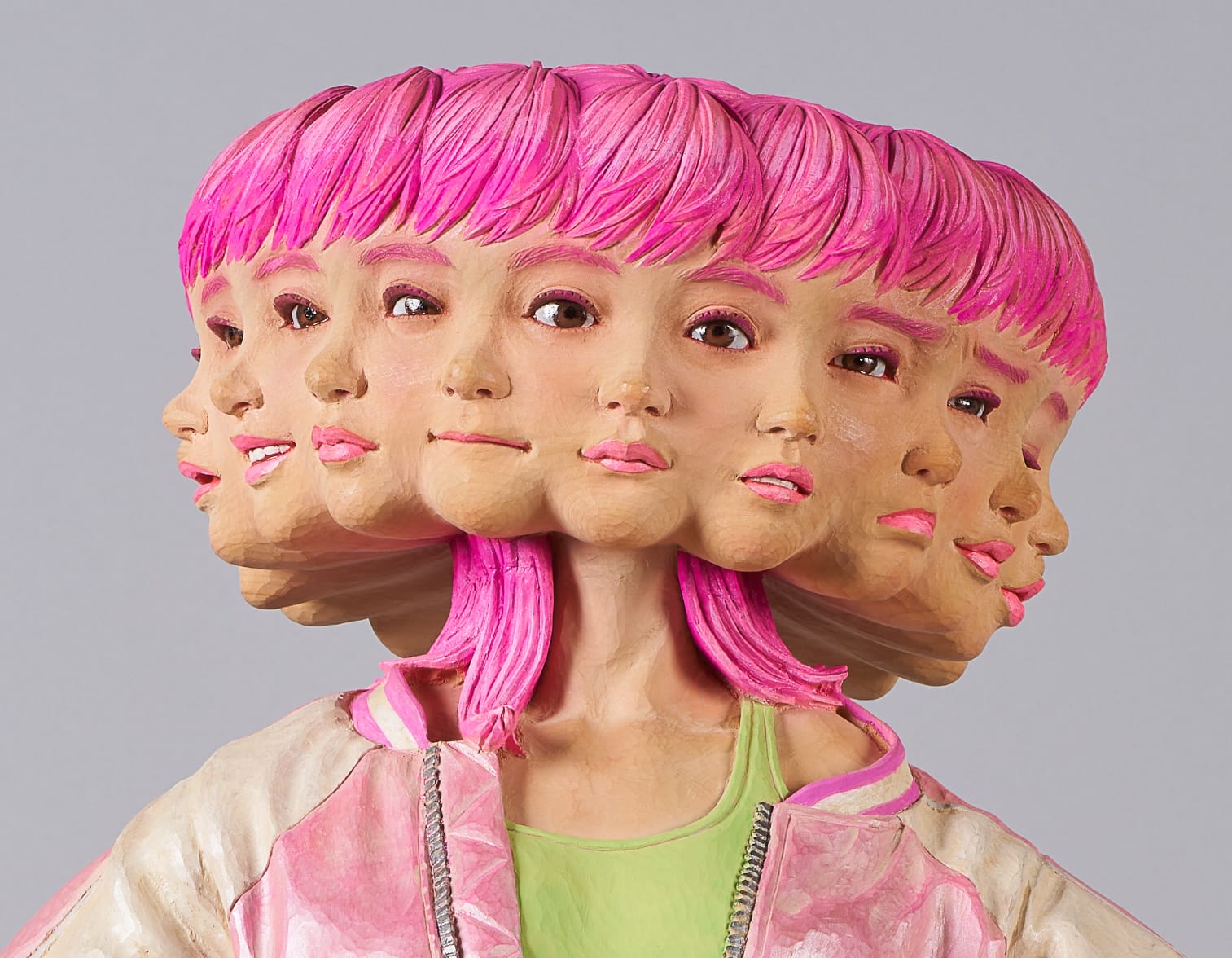 a detail of a wooden sculpture by Yoshitoshi Kanemaki of a female figure with bright pink shorts and a jacket, with multiple faces and expressions