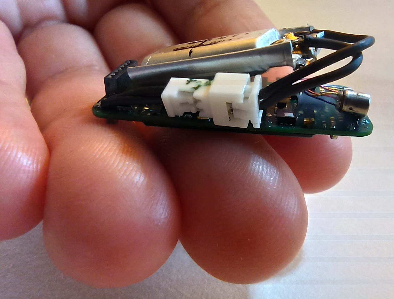 Miniature biologging backpack being held by fingers.