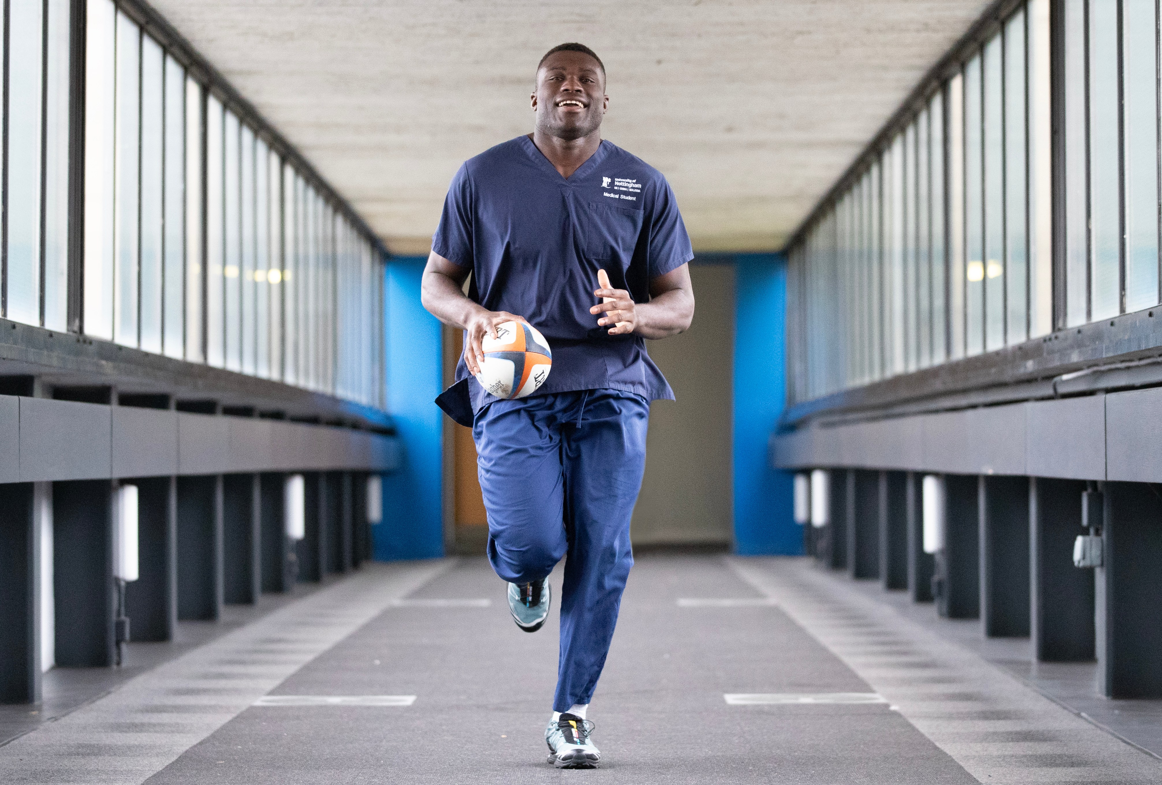 Leicester Tigers player and medical student, Emeka Ilione, runs through a tunnel while holding a rugby ball.