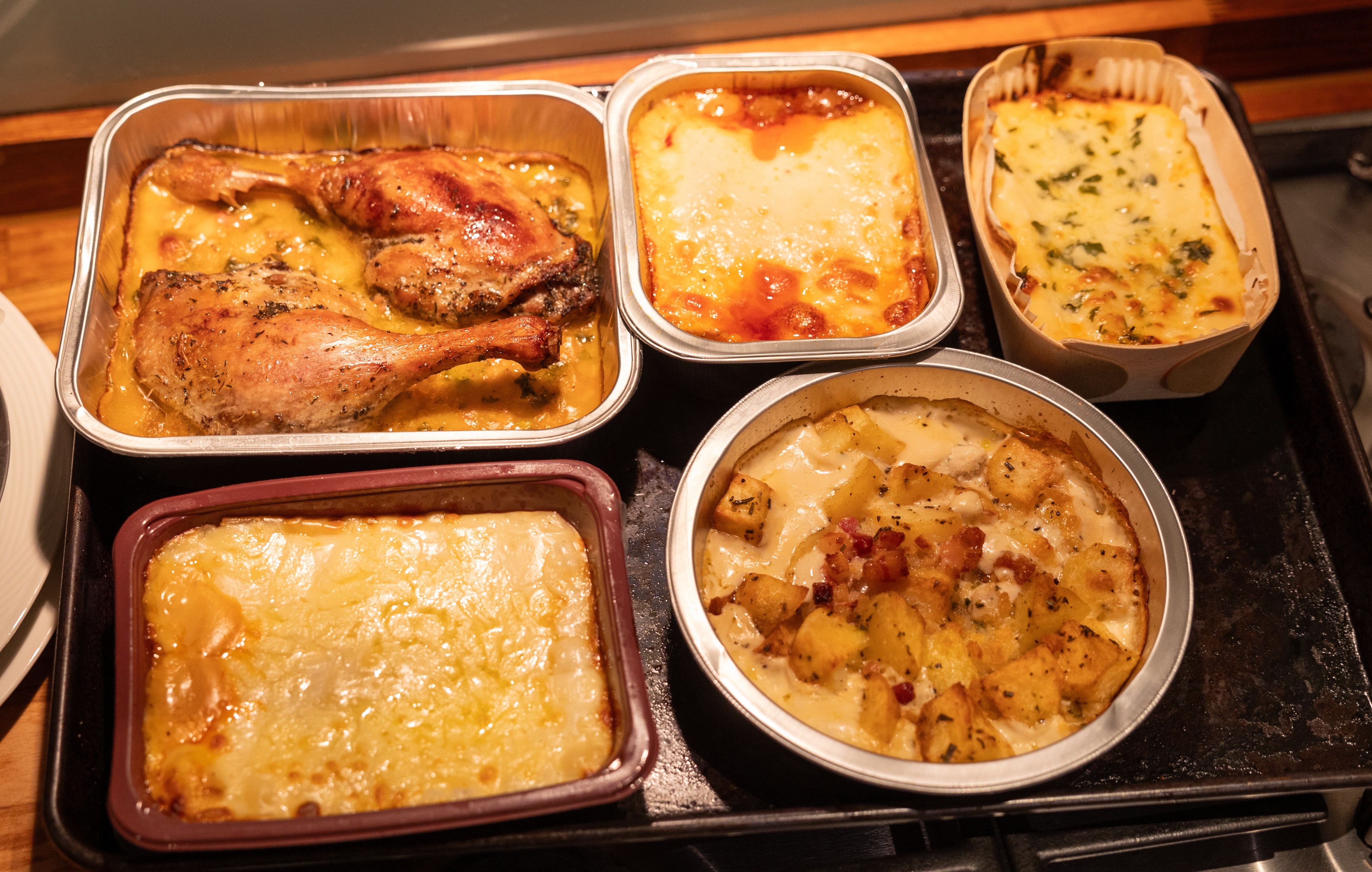 An assortment of ready meals for a dinner party, including duck legs, lasagna, and potato gratin, on a metal tray.