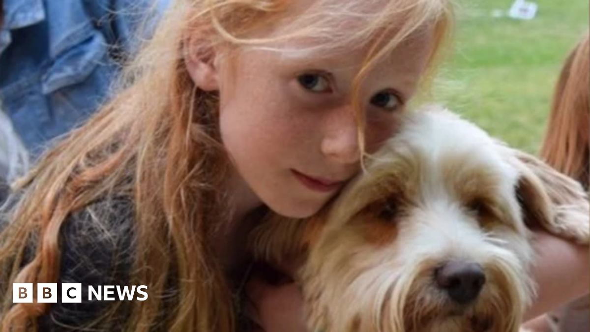 A picture of Ruth Szymankiewicz, who has long ginger hair, cuddling a terrier dog.