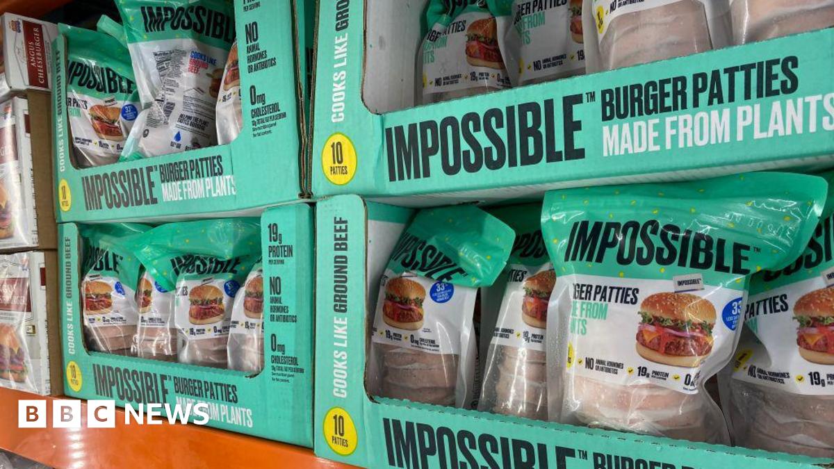 Four bright green boxes of "Impossible" burger patties on a shelf in the supermarket. The box is also labelled that it is "made from plants".