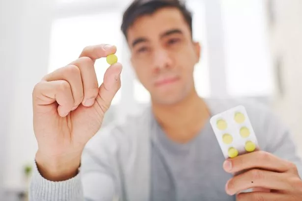 Young man holding round yellow pill