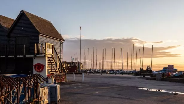 Whitstable taken at dusk. Orange sun in distance  Lifeboat house and sailing boats moored on the beach