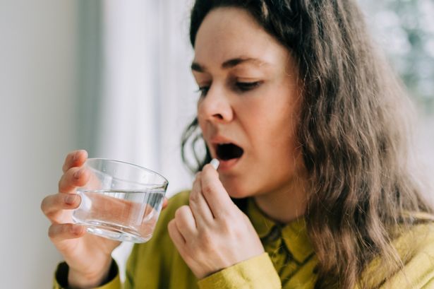 Mid woman taking medicine with glass of water at home