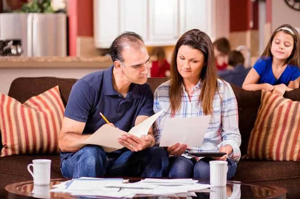 A man and woman sitting down together to work out their finances, with invoices on the living room table and children in the background