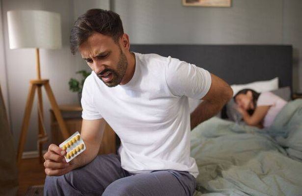 Man suffering from back pain while holding painkillers in bedroom
