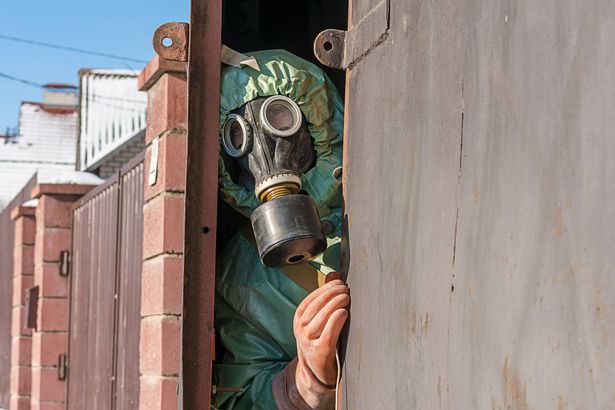 Person in protective suit looking through open iron gate