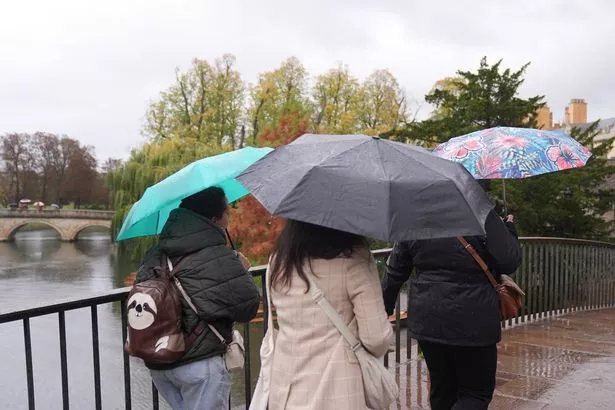 Three people walking over a bridge, using umbrellas to shelter from the rain