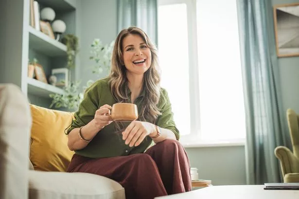 A mature woman siting comfortably on the sofa at home and sipping tea.