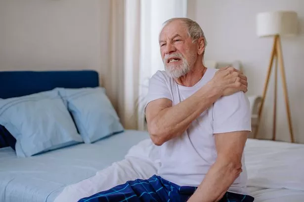 Senior man having pain in shoulder. Sitting alone in his bedroom.