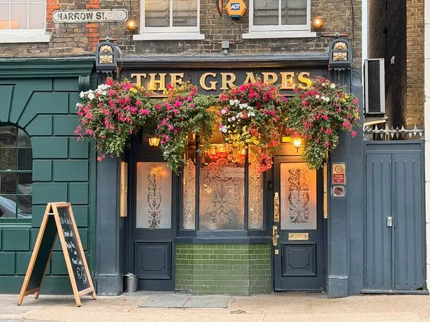 The exterior of Ian McKellen's pub, The Grapes, with colourful hanging baskets and frosted glass