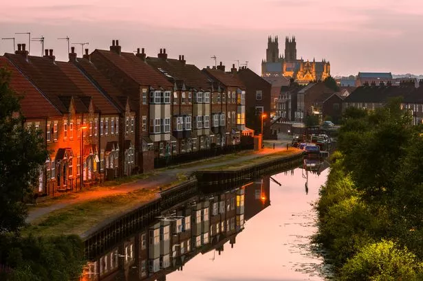 Beverley, Yorkshire, UK. The Minster just after sunset with view of the beck (canal) flanked by modern town houses and barges with reflections in Beverley, Yorkshire, UK.