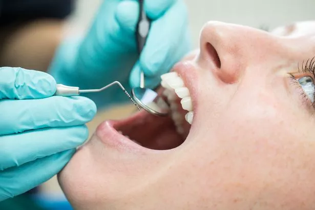 Close up of dentist holding angled mirror and hook while examining patient. Young woman is with mouth open getting dental check-up in hospital.