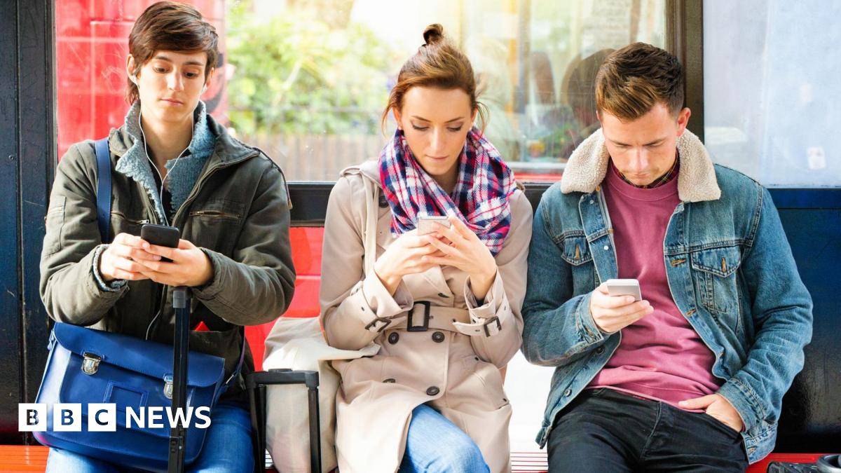 Three people sitting at a bus stop looking at their mobile phones