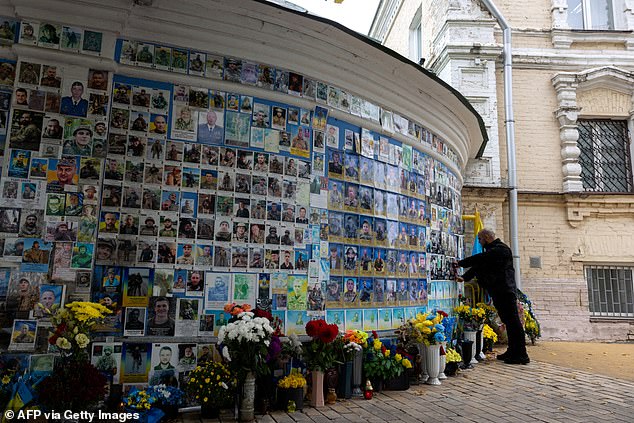 A man touches a photograph of his deceased comrade on the Wall of Remembrance of the Fallen for Ukraine, a memorial dedicated to Ukrainian soldiers, on Defender's Day of Ukraine in Kyiv, on October 1, 2025, amid the Russian invasion of Ukraine
