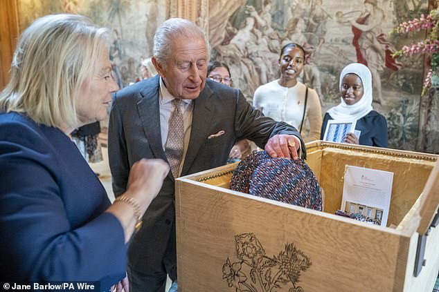 The King is pictured while peering inside a time capsule - which will be buried for a century in early 2026